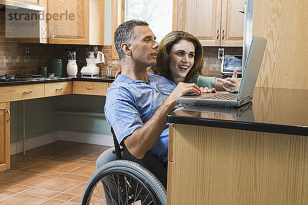 Mid adult couple with man in a wheelchair looking at a laptop and smiling