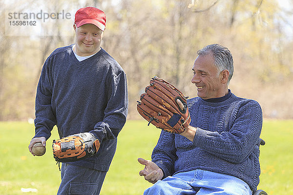 Vater mit Rückenmarksverletzung und sein Sohn mit Down-Syndrom spielen Baseball im Park