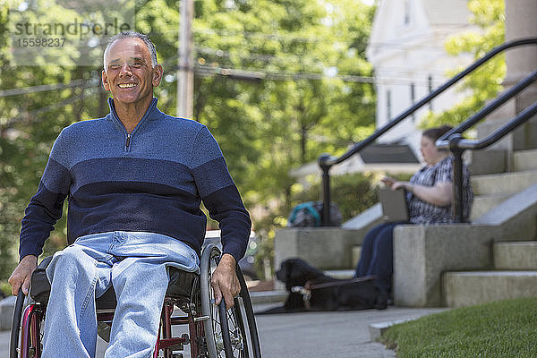 Mann mit Rückenmarksverletzung sitzt im Rollstuhl mit seiner blinden Tochter im Hintergrund