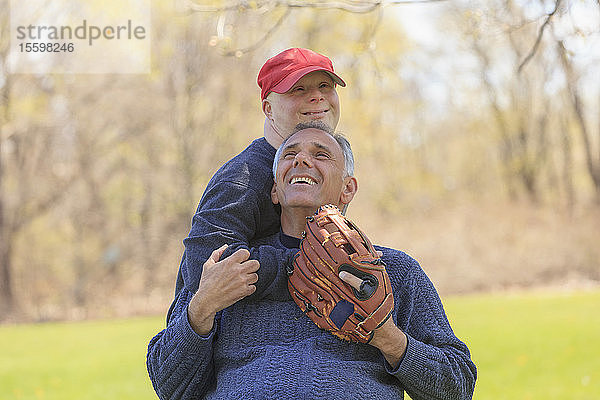 Glücklicher Vater mit Rückenmarksverletzung und sein Sohn mit Down-Syndrom beim Baseballspielen im Park