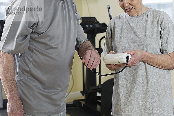 Eine ältere Ehefrau kontrolliert den Blutdruck ihres Mannes im Fitnessstudio.