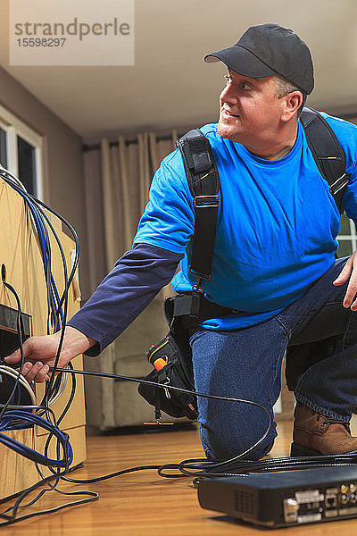 Kabelinstallateur bei der Arbeit in einer Wohnung hinter dem Fernseher