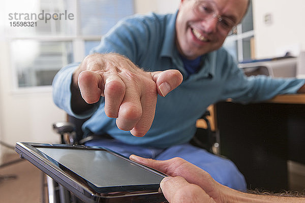 Zwei behinderte Männer  die in Rollstühlen sitzen und ein digitales Tablet benutzen  einer mit deformierten Händen