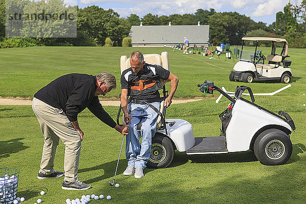 Mann mit Rückenmarksverletzung in einem adaptiven Wagen auf dem Golf-Putting-Green mit einem Ausbilder