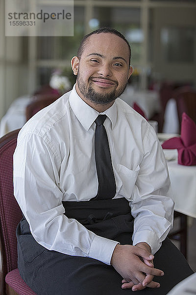 Porträt eines glücklichen afroamerikanischen Mannes mit Down-Syndrom als Kellner in einem Restaurant