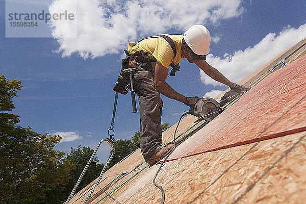 Spanischer Zimmermann bei der Arbeit mit einer Kreissäge an einer Dachschalung in einem im Bau befindlichen Haus