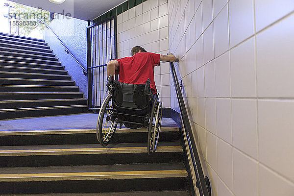 Trendiger Mann mit einer Rückenmarksverletzung im Rollstuhl  der rückwärts eine U-Bahn-Treppe hinunterfährt