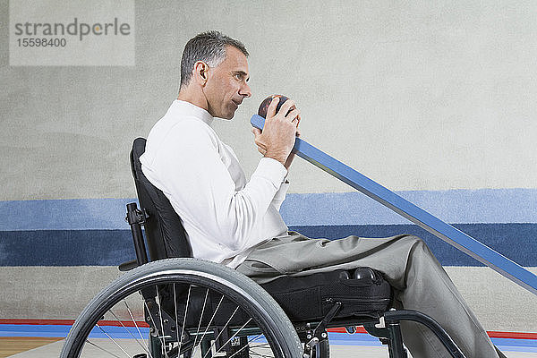 Seitenprofil eines reifen Mannes mit einer Rückenmarksverletzung  der in einem Rollstuhl sitzt und Ten-Pin-Bowling spielt