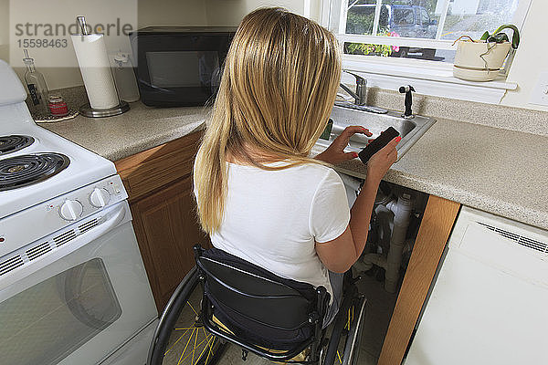 Frau mit Rückenmarksverletzung in ihrer barrierefreien Küche  die ein Mobiltelefon benutzt