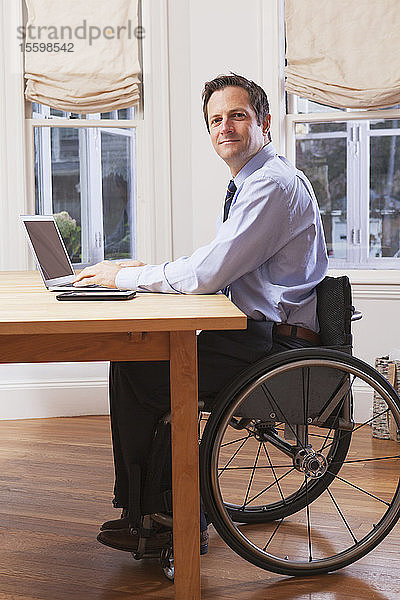 Geschäftsmann mit Querschnittslähmung im Rollstuhl bei der Arbeit am Laptop