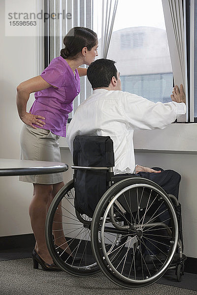 Geschäftsmann mit Rückenmarksverletzung und Geschäftsfrau schauen durch ein Fenster