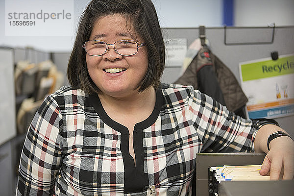 Asiatische Frau mit einer Lernbehinderung benutzt einen Aktenschrank im Büro