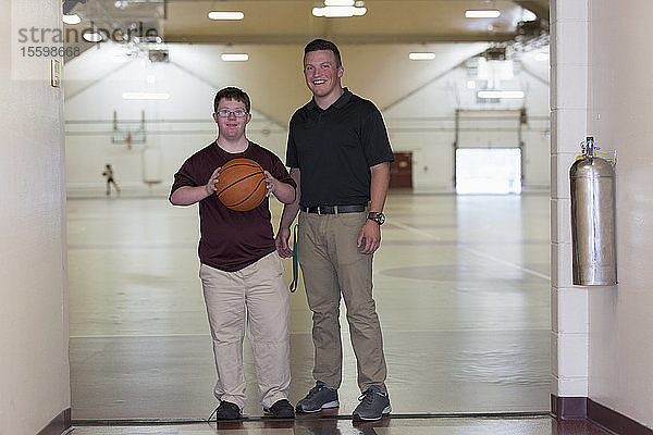 Junger Mann mit Down-Syndrom spielt mit seinem Freund in der Turnhalle der Schule Basketball