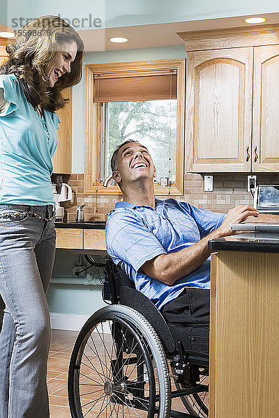 Mittlerer erwachsener Mann  der in einem Rollstuhl sitzt und eine mittlere erwachsene Frau lächelnd anschaut