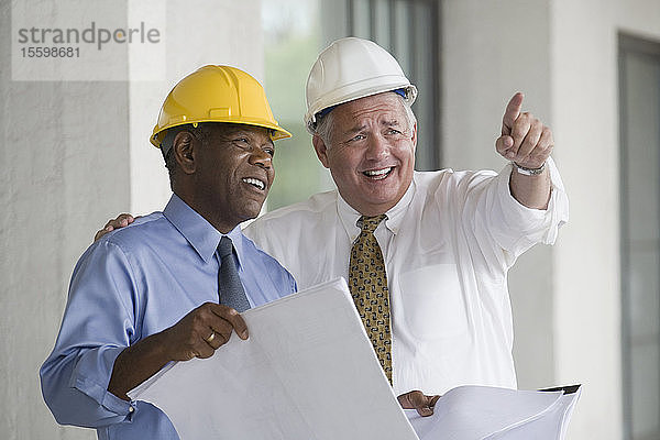 Zwei Ingenieure diskutieren einen Bauplan und lächeln
