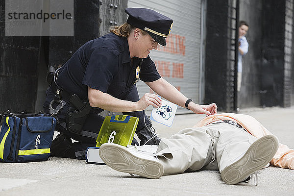Polizeibeamtin verabreicht einem älteren Mann einen Defibrillator