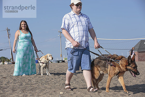 Ein blindes Paar geht mit seinen Diensthunden am Strand entlang