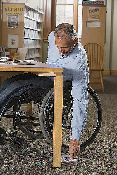 Ein Mann im Rollstuhl mit einer Rückenmarksverletzung greift in einer Bibliothek nach DVDs