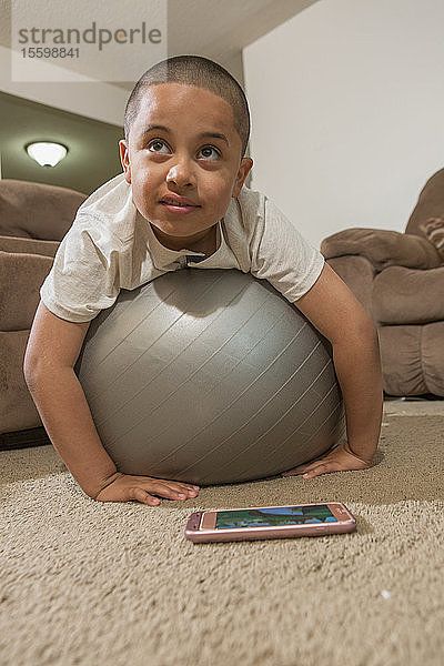 Hispanischer Junge mit Autismus spielt mit einem Gymnastikball im Wohnzimmer