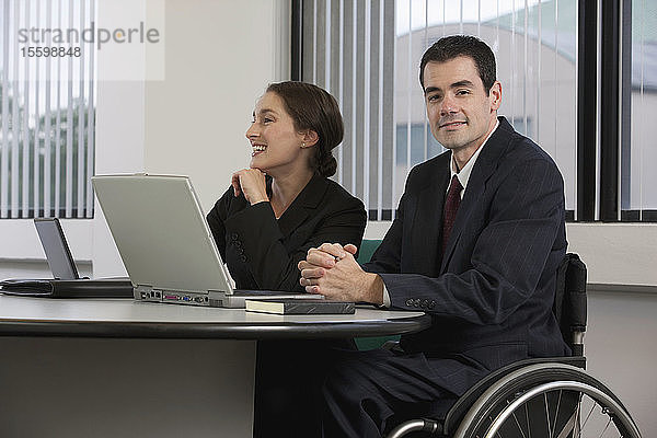 Geschäftsmann mit Rückenmarksverletzung arbeitet mit einer Geschäftsfrau an einem Laptop