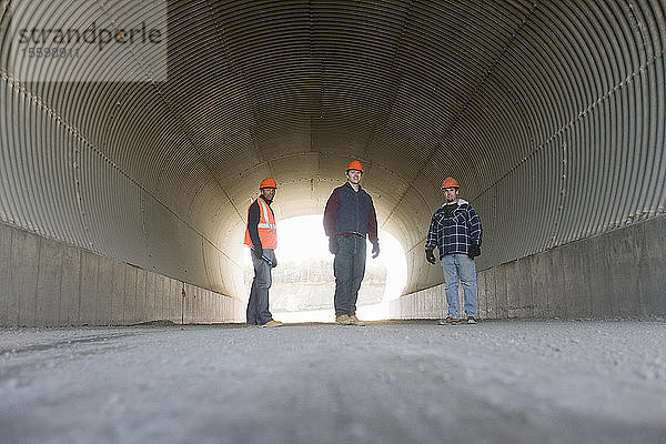 Drei Ingenieure stehen in einem Tunnel eines Asphaltwerks