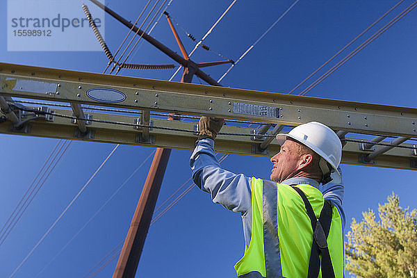 Ingenieur stellt Leiter auf  um Geräte an Strommasten zu installieren