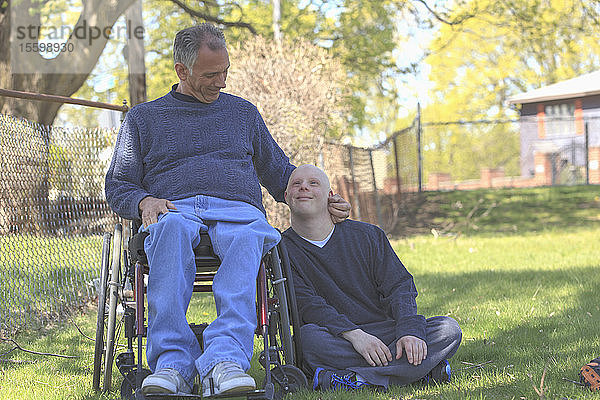 Glücklicher Vater mit Rückenmarksverletzung und sein Sohn mit Down-Syndrom in einem Park