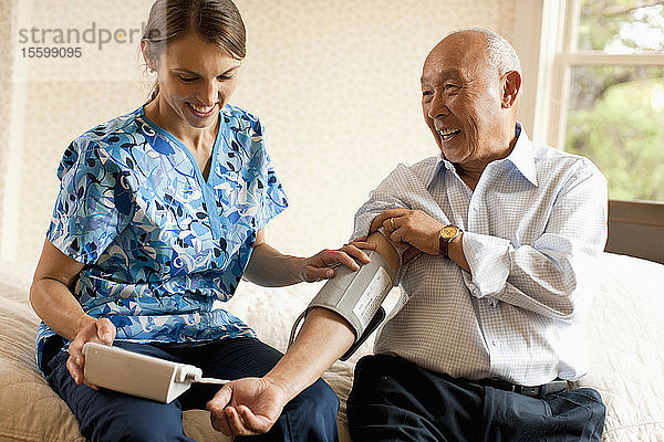 Ein älterer Mann lässt seinen Blutdruck von einer Krankenschwester zu Hause überprüfen