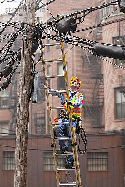 Ein Kabelmonteur klettert auf einer Leiter auf einen Strommast