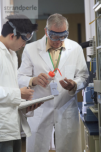 Ein Professor arbeitet mit einem Ingenieurstudenten zusammen  der Ethanol in ein Probentablett in einem Labor einfüllt.