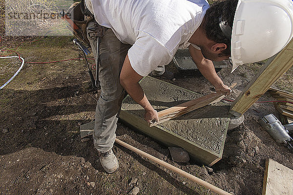 Hispanischer Zimmermann beim Nivellieren von Beton im Treppenfundament