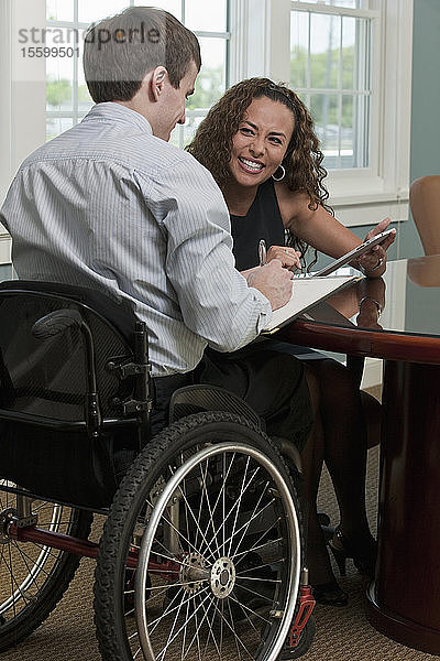 Geschäftsmann mit Rückenmarksverletzung und eine sehbehinderte hispanische Geschäftsfrau diskutieren in einem Büro