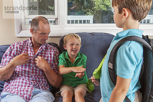 Vater und Söhne mit Hörbehinderung gebärden Schule  Rucksack in amerikanischer Zeichensprache auf ihrer Couch