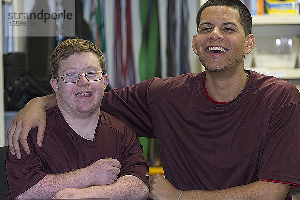 Junger Mann mit Down-Syndrom amüsiert sich mit dem Betreuer in der Ausgabestelle für Hochschulausrüstung