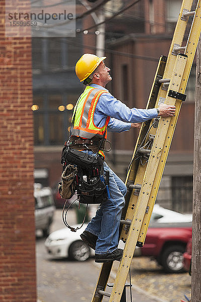 Ein Kabelmonteur klettert eine Leiter auf einem städtischen Gebäude hoch