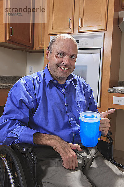 Mann mit Friedreich-Ataxie  der mit seinen deformierten Händen eine Tasse Wasser hält