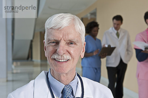 Lächelnder Arzt mit seinen Kollegen im Hintergrund