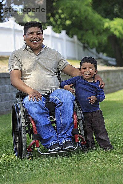 Porträt eines hispanischen Mannes mit Rückenmarksverletzung im Rollstuhl mit seinem Sohn im Rasen