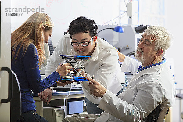 Professor mit Muskeldystrophie bei der Arbeit mit Ingenieurstudenten  die eine verstellbare Bühne an einem chemischen Analysegerät in einem Labor einrichten