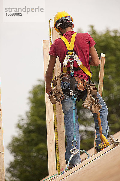 Ein spanischer Zimmermann misst ein Brett auf dem Dach eines im Bau befindlichen Hauses aus