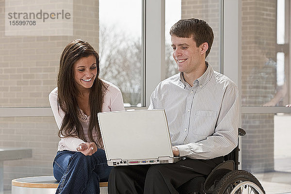 Lehrer mit Rückenmarksverletzung und ein Schüler  der einen Laptop benutzt