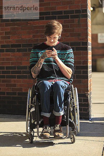 Trendiger Mann mit einer Rückenmarksverletzung im Rollstuhl  der seine Textnachrichten entgegennimmt