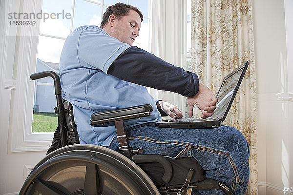 Mann mit Rückenmarksverletzung im Rollstuhl arbeitet mit seinen behinderten Händen an einem Laptop