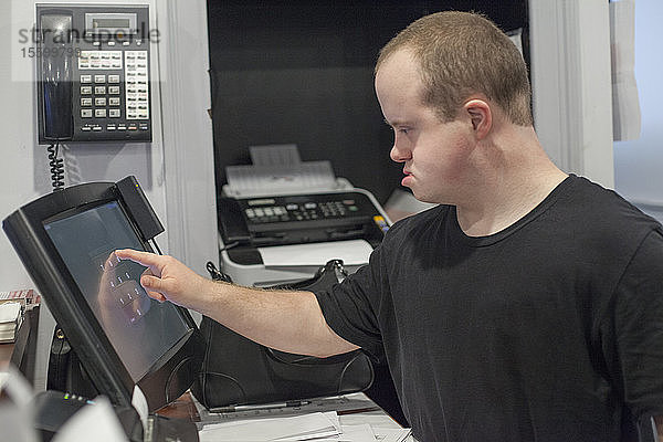 Kellner mit Down-Syndrom bei der Eingabe eines Verkaufs am Computer im Büro
