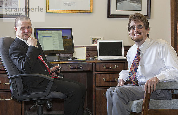 Mann mit Down-Syndrom lächelt mit einem Mitarbeiter im State Capitol in seinem Büro