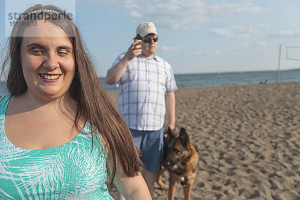 Ein blindes Paar  das mit seinem Diensthund am Strand spazieren geht und dabei seine Hilfsmittel benutzt