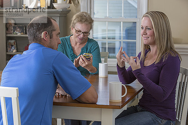 Drei Personen bei einem Treffen und zwei  die sich in ASL über Familie zu Hause unterhalten