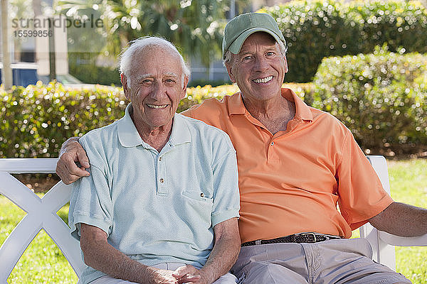 Porträt von zwei älteren Männern  die auf einer Parkbank sitzen und lächeln