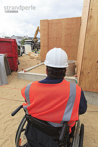 Bauingenieur mit Rückenmarksverletzung beobachtet  wie ein Bagger einen Kipplaster füllt