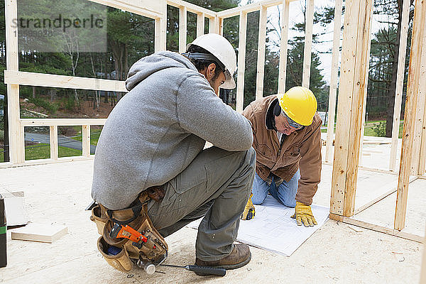 Ein Bauleiter bespricht mit einem Zimmermann den Bauplan eines Hauses